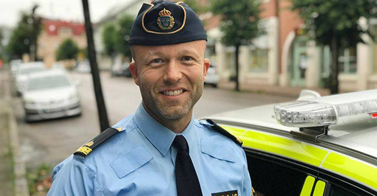 Polismannen Kristoffer står i uniform på en gata och ler mot kameran