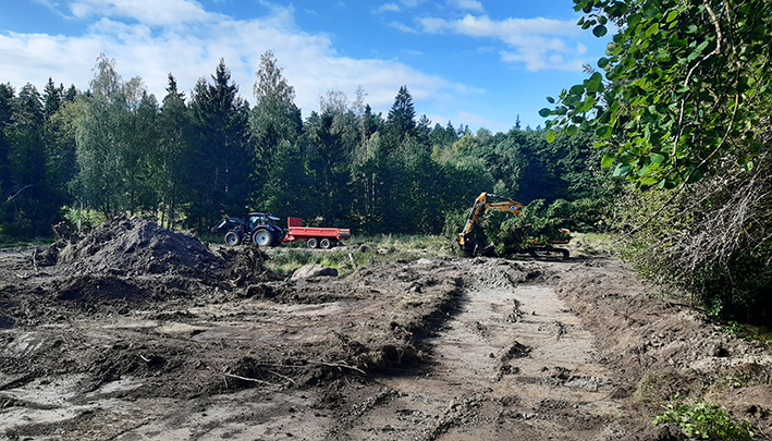 Grävmaskin och traktor som står på en större yta där jord grävts fram