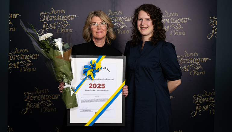 Två kvinnor framför en fotovägg med texten Årets Företagarfest. En av kvinnorna håller i ett diplom och en blombukett.