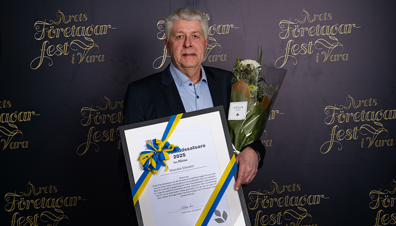 En man i kostym som håller i ett diplom och en blombukett.