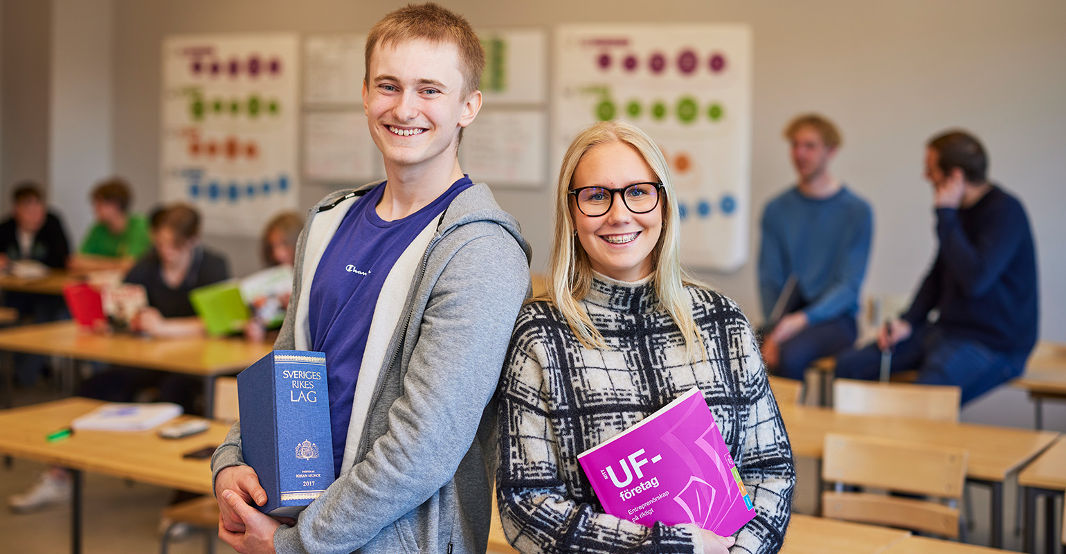 Två elever i klassrum som håller i kurslitteratur.