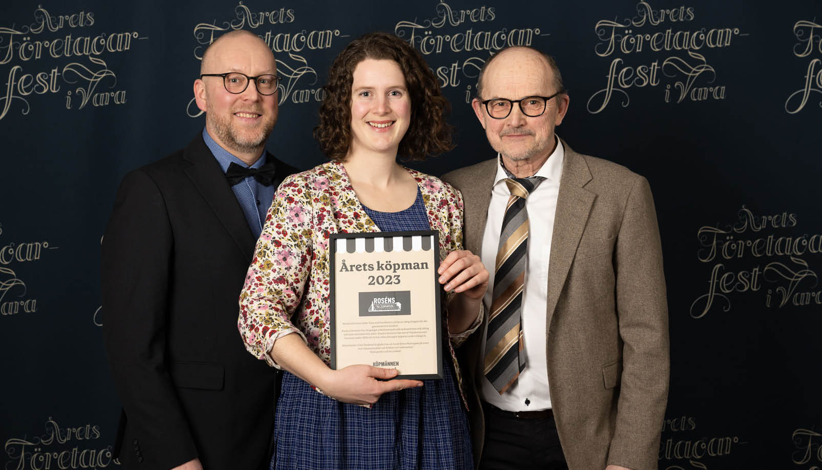 En kvinna och två män i kostym, kvinnan i mitten håller i ett diplom.