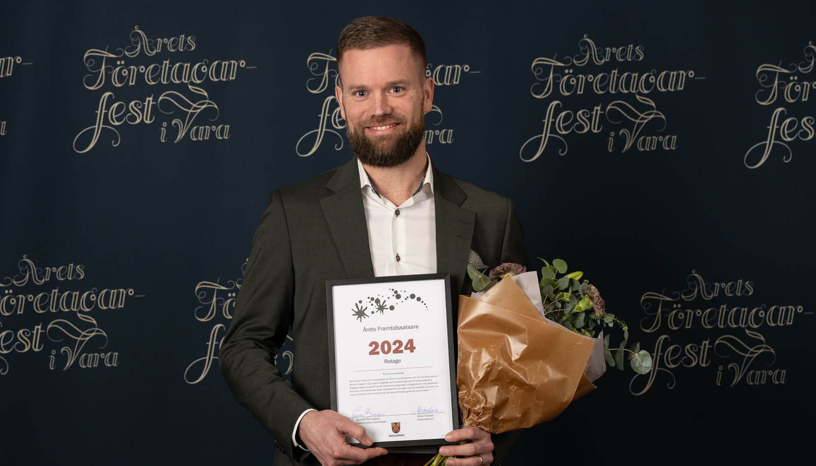 En man i kostym som håller i ett diplom och en blombukett.