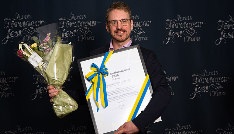 En man i kostym som håller i ett diplom och en blombukett.