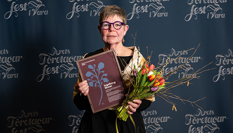 En kvinna med diplom och blommor i händerna.