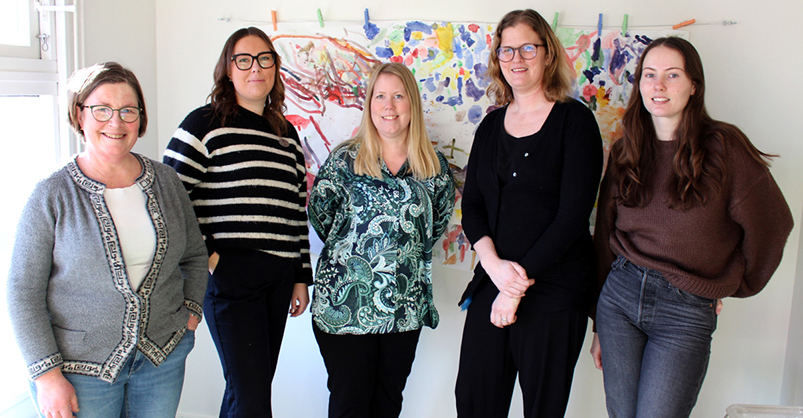 Fem kvinnor står bredvid varandra. I bakgrunden finns en färgglad tavla från Ugglans konst