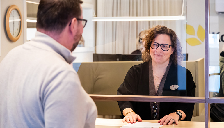 Besökare står vid en receptionsdisk och pratar med personal bakom glasruta.